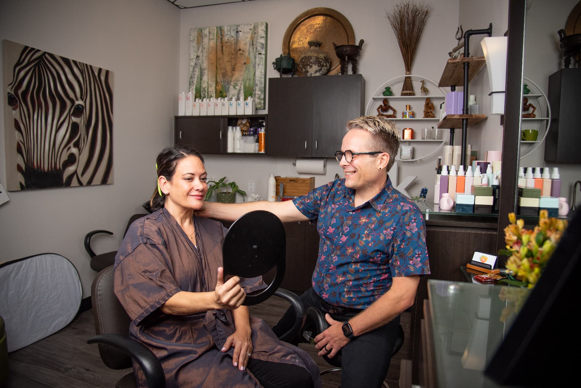 Ray and a seated client looking over her hair together in a hand mirror.