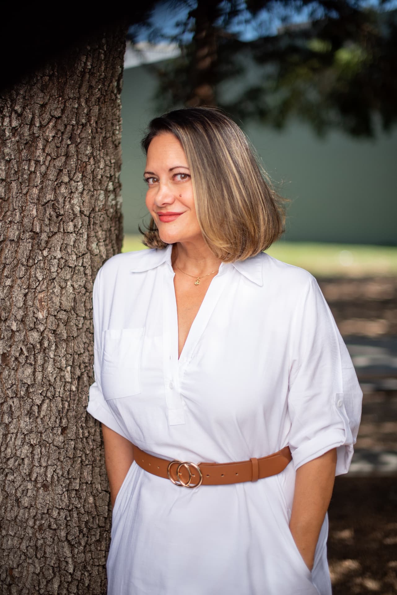A glowing guest with a glossy, dimensional bob, smiling beside an oak tree.